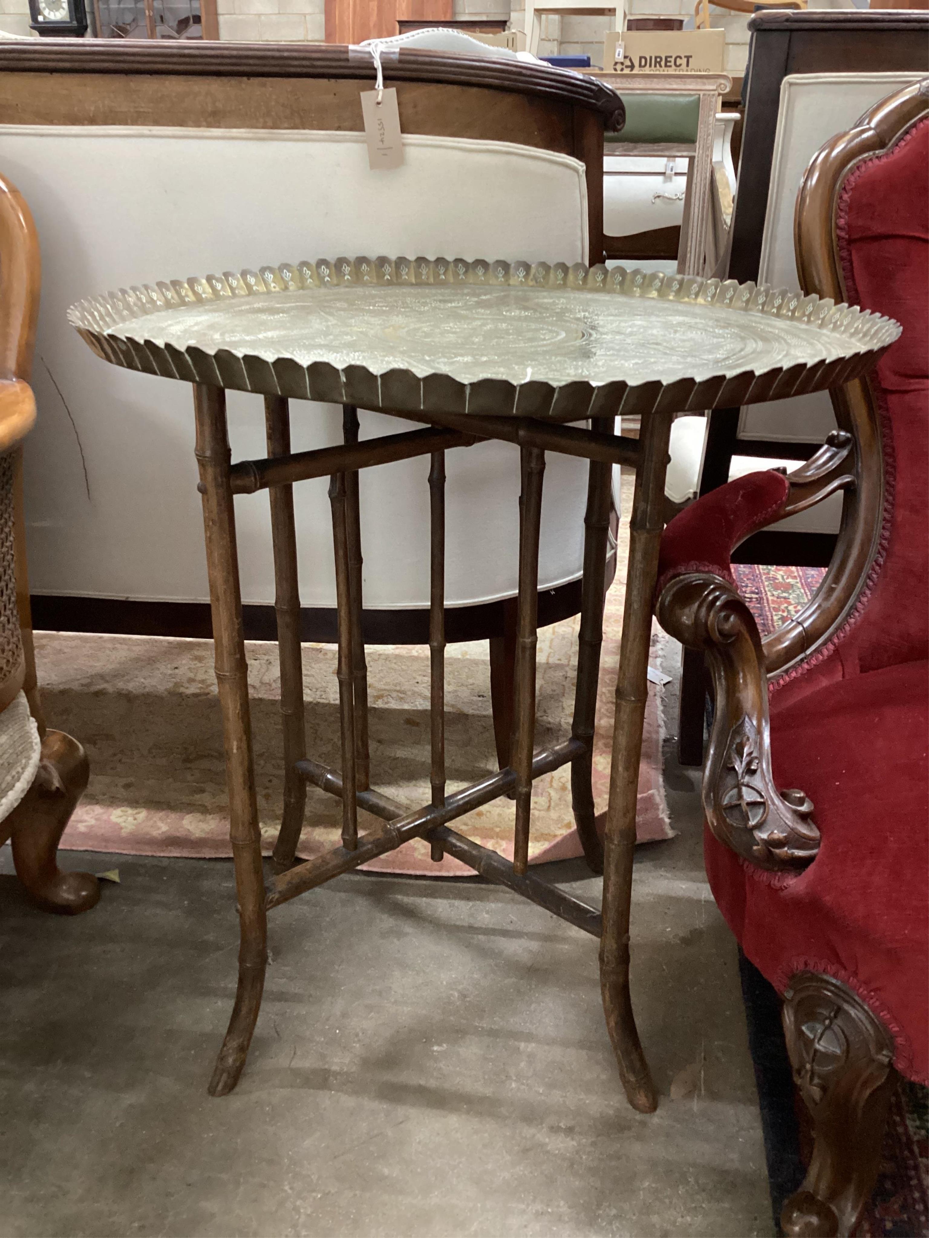 An early 20th century circular engraved brass tray top table on folding bamboo stand, diameter 64cm, height 72cm. Condition - fair